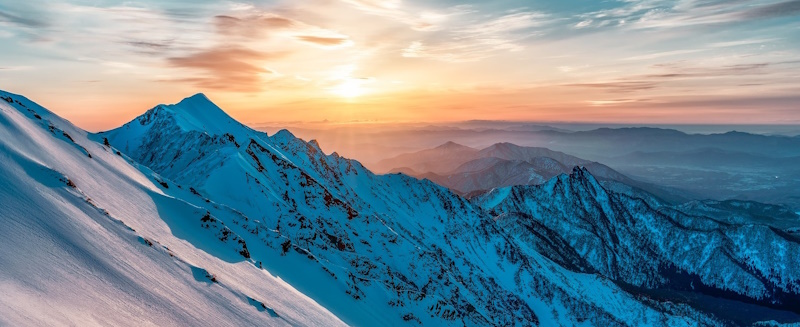 Beautiful snowy peaks with the sun setting in the distance.