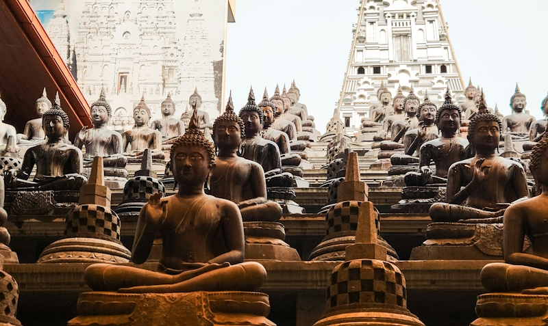 Many Buddha statues interspersed with rupas on an inclined religious site.
