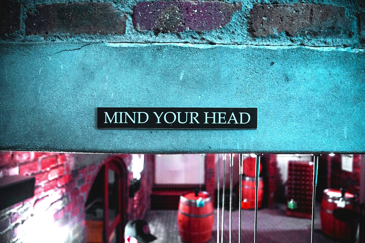 A low cement ceiling overhang as you walk down a set of stairs with a sign on it saying mind your head.