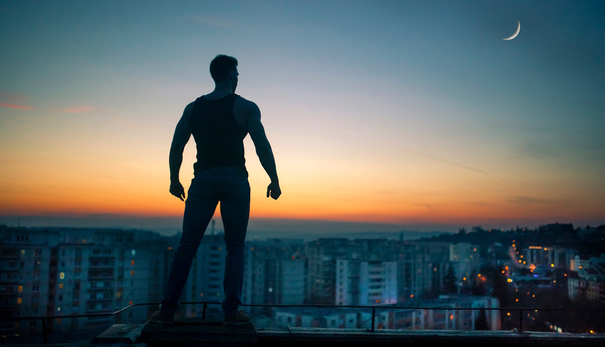 Strongly built man gazing at the sunrise from a roof top.