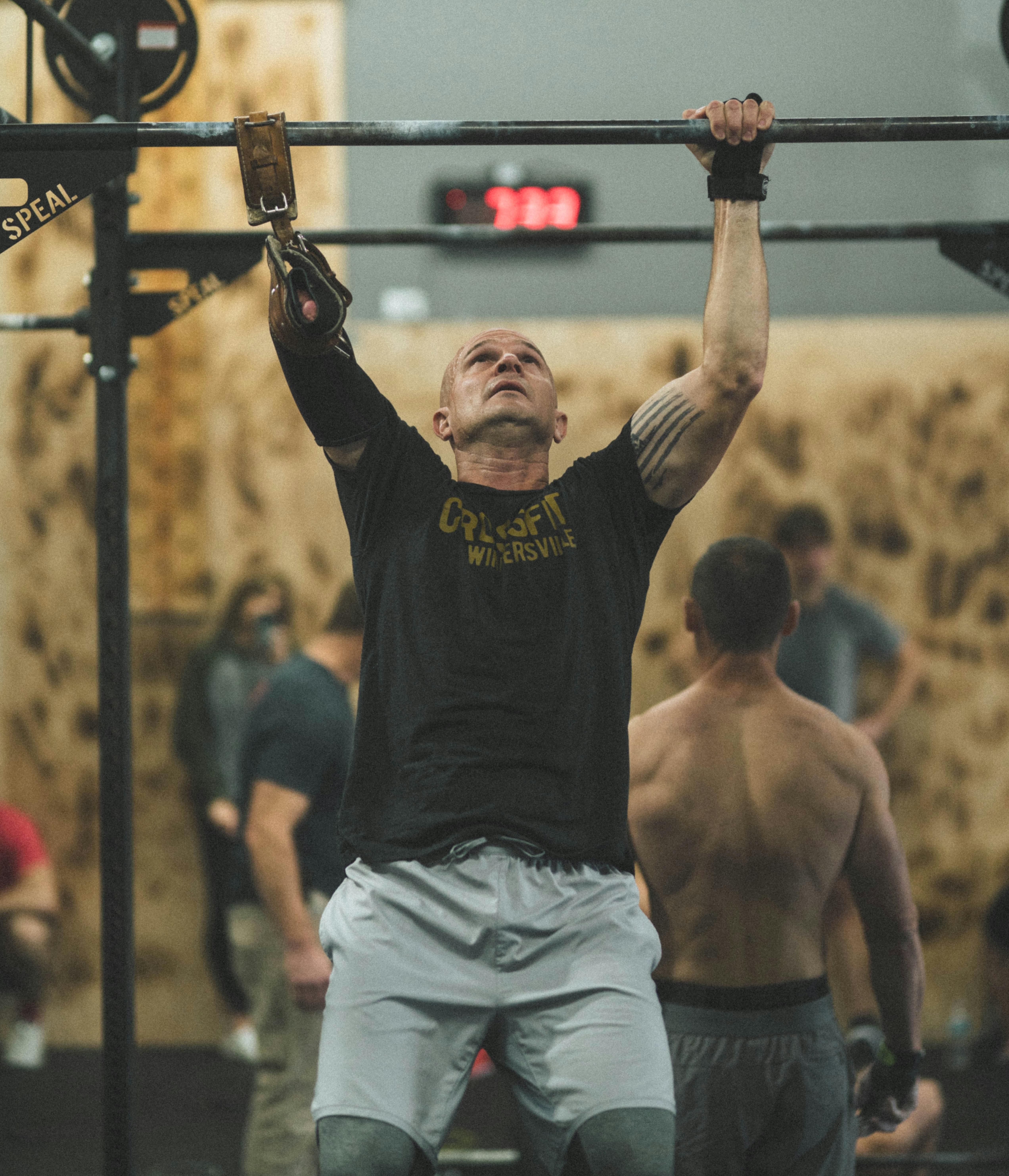 A one-armed man with a brace on his missing arm doing chin ups in the gym.