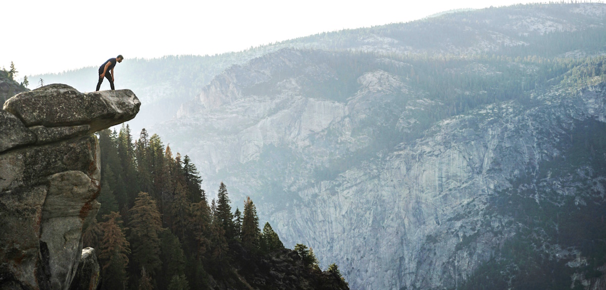 A man carefully looking over a cliff in the mountains.